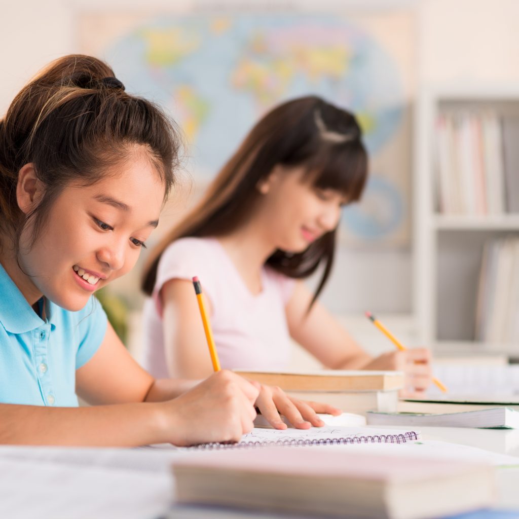 Students studying together in a bright classroom, focused on JC Economics exam preparation and active learning.
